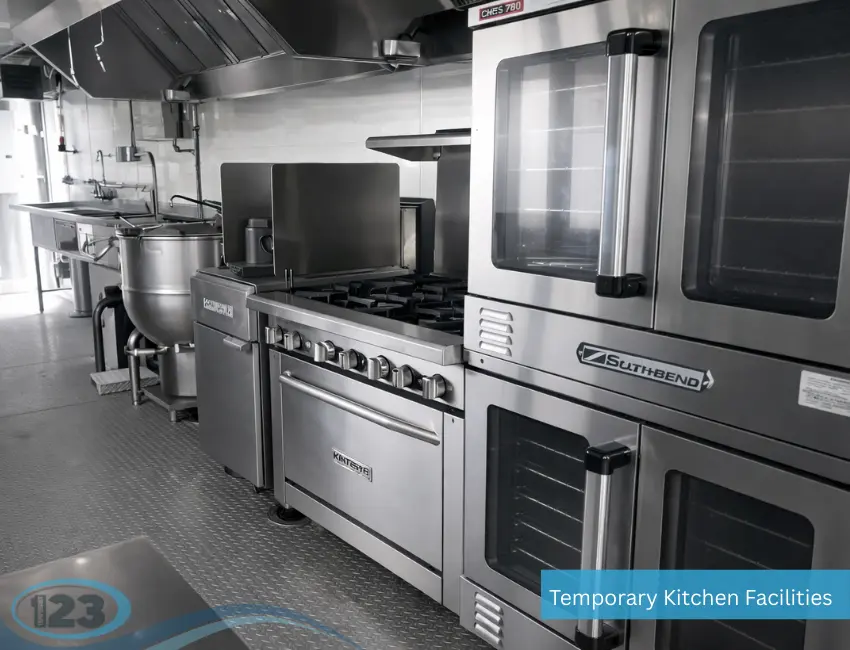 An interior view of a commercial temporary kitchen facility featuring double-stacked Southbend industrial ovens, a Kintera gas stove range with open burners, a large tilting kettle, and stainless steel prep sinks on diamond plate flooring.