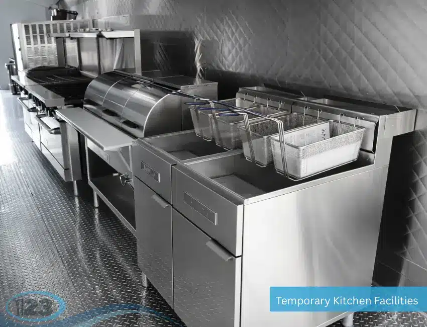 Interior line of a commercial temporary kitchen facility featuring two industrial stainless steel deep fryers with wire baskets hanging on the racks, positioned next to a flat top grill and diamond plate flooring.
